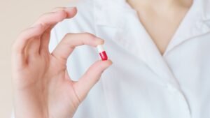 Persona con bata blanca mostrando una cápsula roja y blanca, representando la profesión farmacéutica